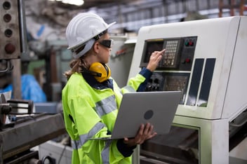 Frau an der CNC-Maschine mit einem Laptop.